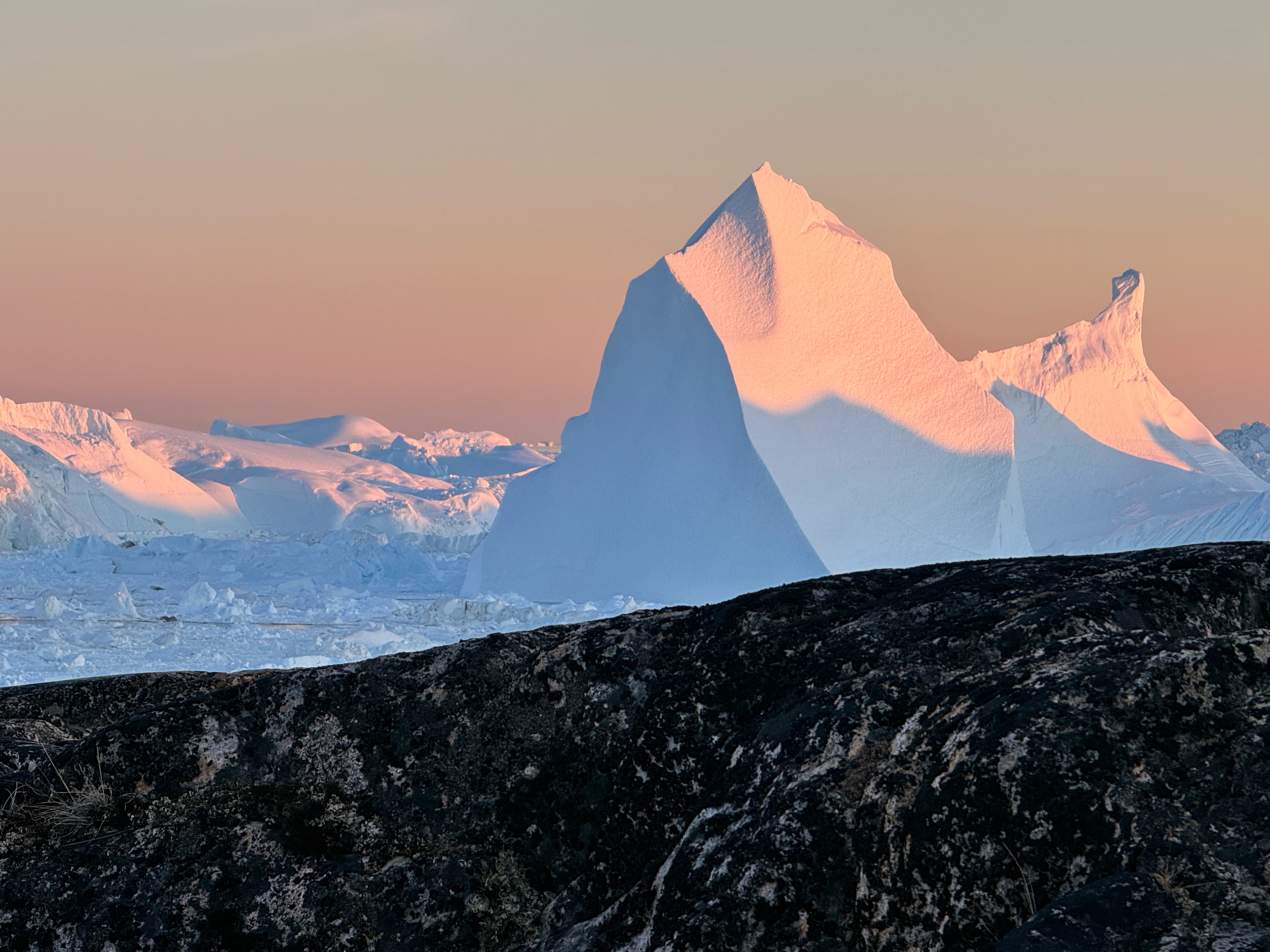 Grounded icebergs in Ilulissat icefjord washed in evening pastel.